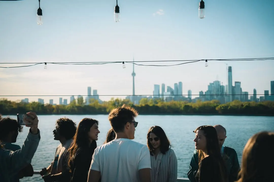Guests in pyjamas crowded on a yacht deck with the Toronto skyline behind them at dusk